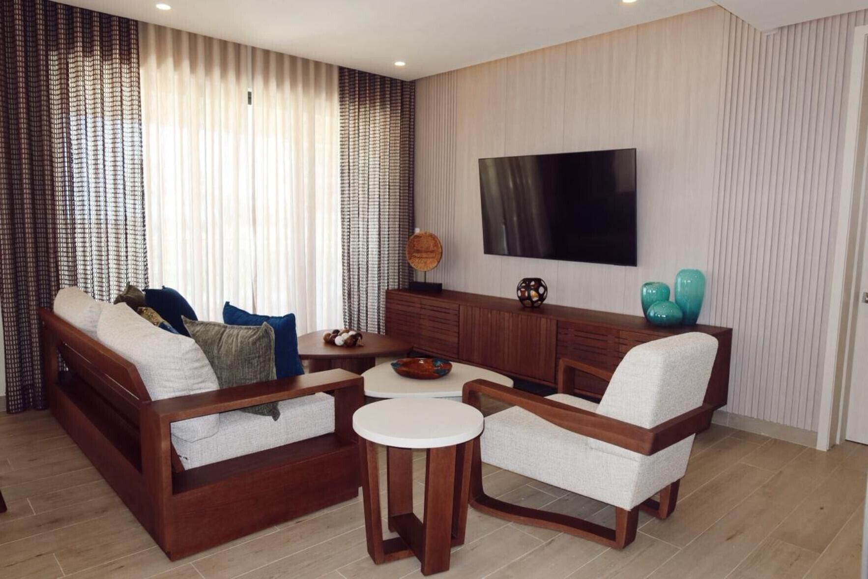 A modern living room with a sofa, two armchairs, a coffee table, and a flat-screen TV mounted on the wall.