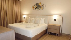 Een hotelkamer met een groot bed, twee nachtkastjes, een decoratief wandobject en een gordijn.