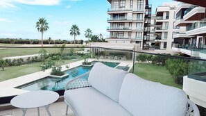Eine moderne Wohnung mit Balkon, Pool und Blick auf umliegende Gebäude und Palmen.