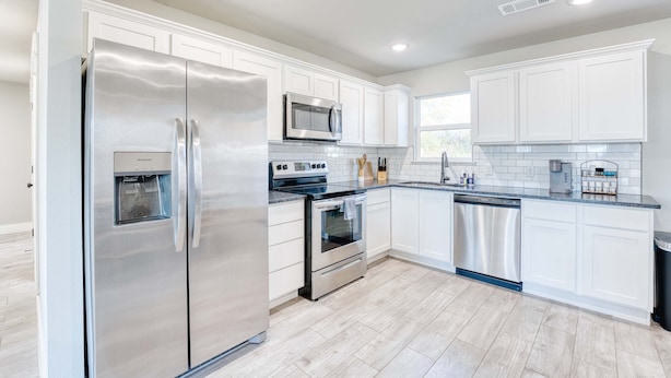 A modern kitchen with white cabinets, stainless steel appliances, and a tiled backsplash. - Modern 4BR Retreat Near Downtown & Trails (Bentonville)