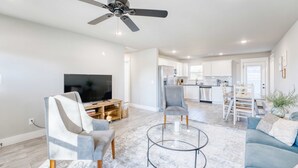 A modern living room with a ceiling fan, a TV, and a seating area with a coffee table. - Modern 4BR Retreat Near Downtown & Trails (Bentonville)