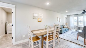 A modern living room with a dining area, featuring a wooden dining table, chairs, a sofa, and a coffee table. - Modern 4BR Retreat Near Downtown & Trails (Bentonville)