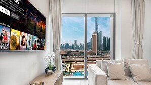 A modern living room with a large window offering a city view, a mounted TV displaying movie posters, and a comfortable sofa. - Stylish 2 bedroom apartment with Burj Khalifa views, connected to Dubai Mall (Dubai)