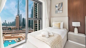 A hotel room with a large window offering a view of the Dubai skyline, including the Burj Khalifa. The room features a bed with white bedding, a bedside table with a lamp, and a wall-mounted artwork. - Stylish 2 bedroom apartment with Burj Khalifa views, connected to Dubai Mall (Dubai)