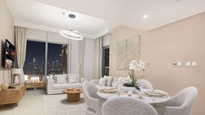 A modern living room with a sofa, dining table set for four, and a city view through large windows. - Stylish 2 bedroom apartment with Burj Khalifa views, connected to Dubai Mall (Dubai)