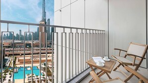 A balcony with a view of the Burj Khalifa and Dubai Mall, a wooden table with a chair, and a white partition. - Stylish 2 bedroom apartment with Burj Khalifa views, connected to Dubai Mall (Dubai)