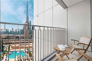 En balkong med utsikt över Burj Khalifa och Dubai Mall, ett träbord med en stol och en vit avskärmning.