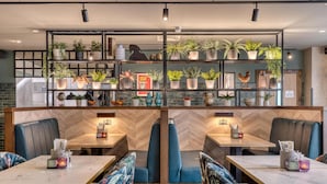 A restaurant interior with booths, a central dining table, and shelves with plants and decorative items. - Premier Inn Hastings Town Centre (Hastings)