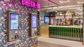 A check-in area with two self-service kiosks, a reception desk, and a neon sign. - Premier Inn Hastings Town Centre (Hastings)