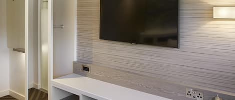 A modern room with a flat-screen TV mounted on a wood-textured wall, a white console table, and a green chair.