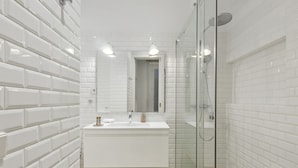 Une salle de bain moderne avec des carreaux de métro blancs, une douche en verre et un meuble-lavabo blanc avec un miroir.