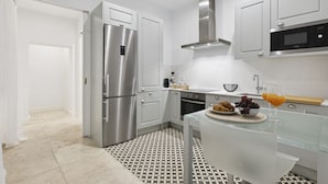 Une cuisine moderne équipée d’appareils électroménagers en acier inoxydable, d’un four à micro-ondes et d’une table à manger en verre, agrémentée d’un panier de fruits et de croissants.
