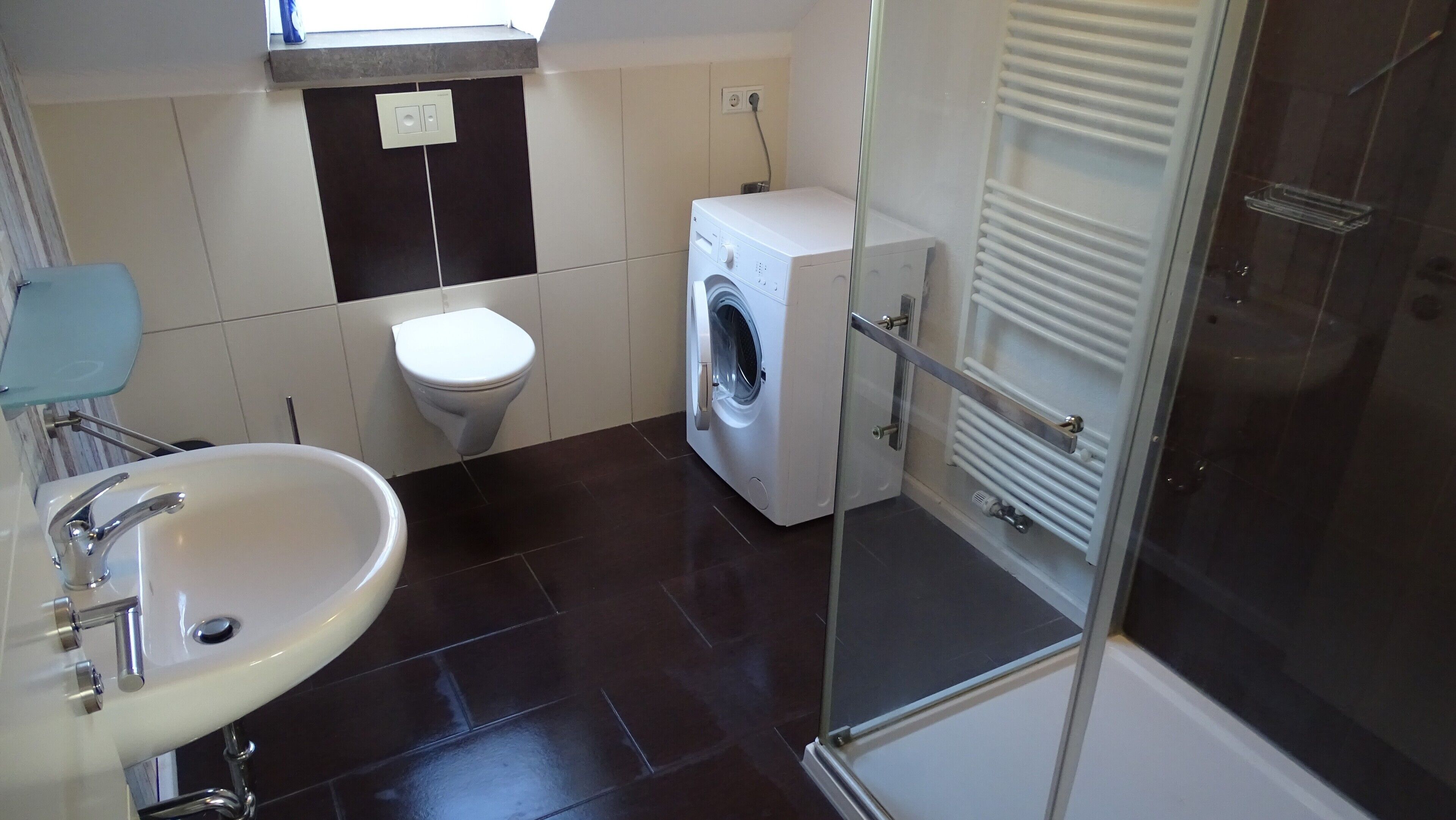 Een badkamer met een wastafel, toilet, wasmachine en een douchecabine van glas.