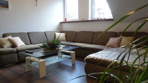 Un salon avec un canapé d’angle, une table basse en verre et une plante.