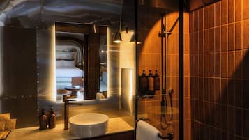 Un baño moderno con ducha envuelta en vidrio, un lavabo redondo y un espejo que refleja un área de sala de estar.