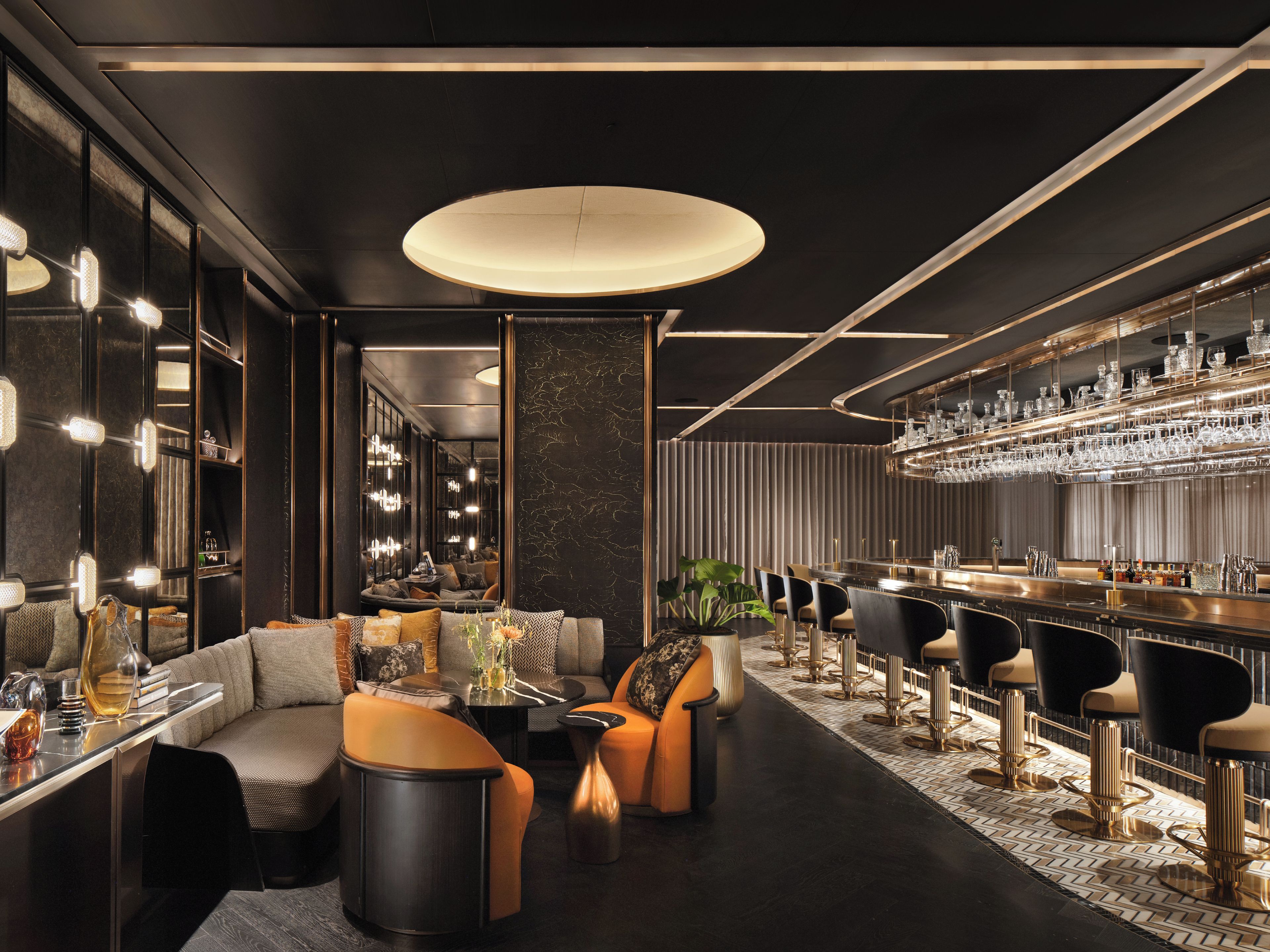 A modern bar area with a long counter, multiple bar stools, and a seating area with sofas and a coffee table.