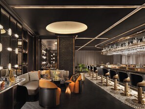 Un espace bar moderne doté d’un long comptoir, de plusieurs tabourets et d’un coin salon avec des canapés et une table basse.