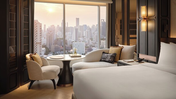 A modern hotel room with a large bed, a round table, two armchairs, and a view of a cityscape through floor-to-ceiling windows. - Fairmont Bangkok Sukhumvit (Bangkok)