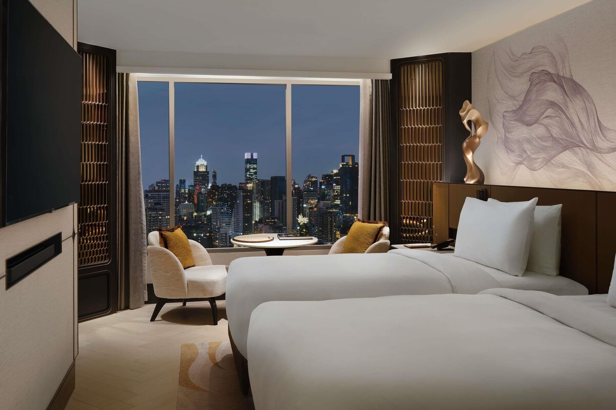Ein Hotelzimmer mit Blick auf die Stadtlandschaft, zwei Betten, einem Sofa und einem kleinen Tisch.
