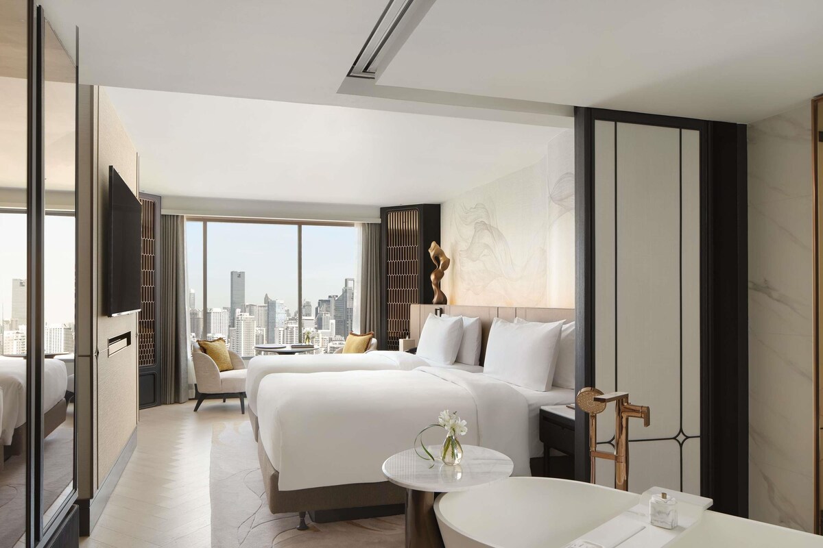 Ein modernes Hotelzimmer mit Blick auf die Stadt, einem großen Bett, einer separaten Sitzecke und einem Badezimmer mit Badewanne.