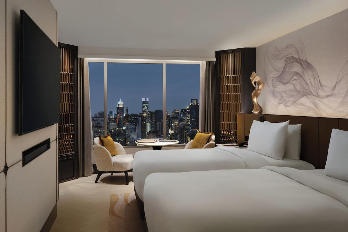 Ein Hotelzimmer mit Blick auf die Stadt, ausgestattet mit zwei Betten, einem Fernseher, einem Schreibtisch und einem Wandbild.