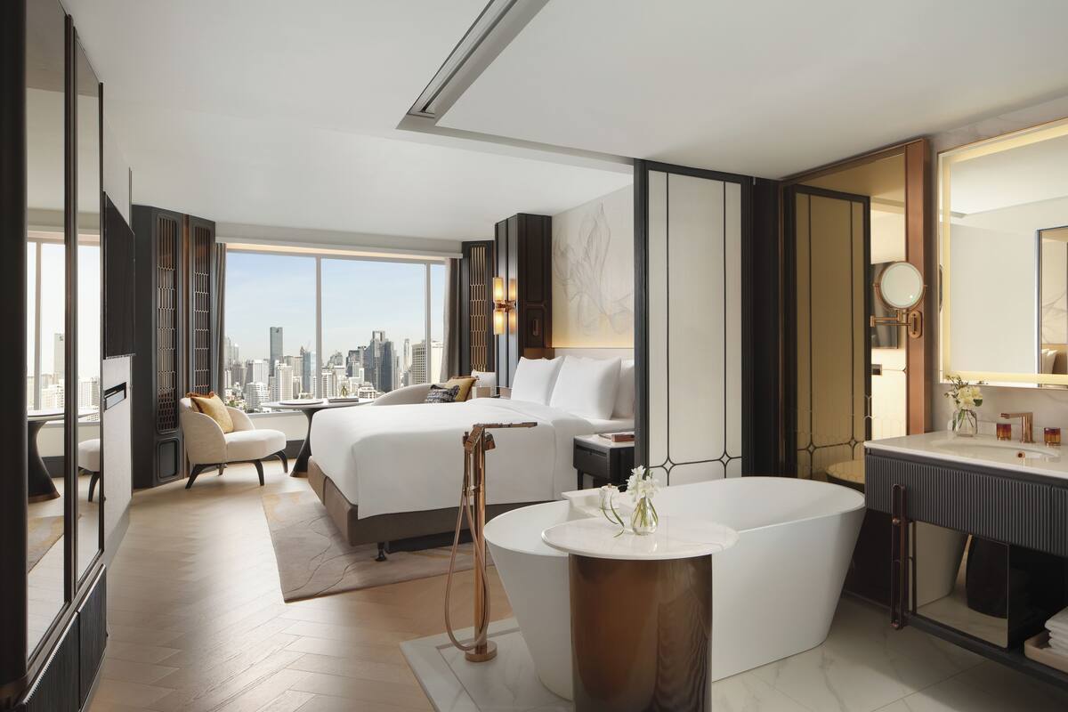 Ein modernes Hotelzimmer mit Blick auf die Stadt, einem großen Bett, einer Sitzecke und einem separaten Badezimmer.