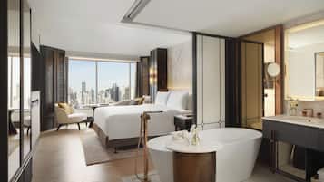A modern hotel room with a city view, a large bed, a sitting area, and a separate bathroom.