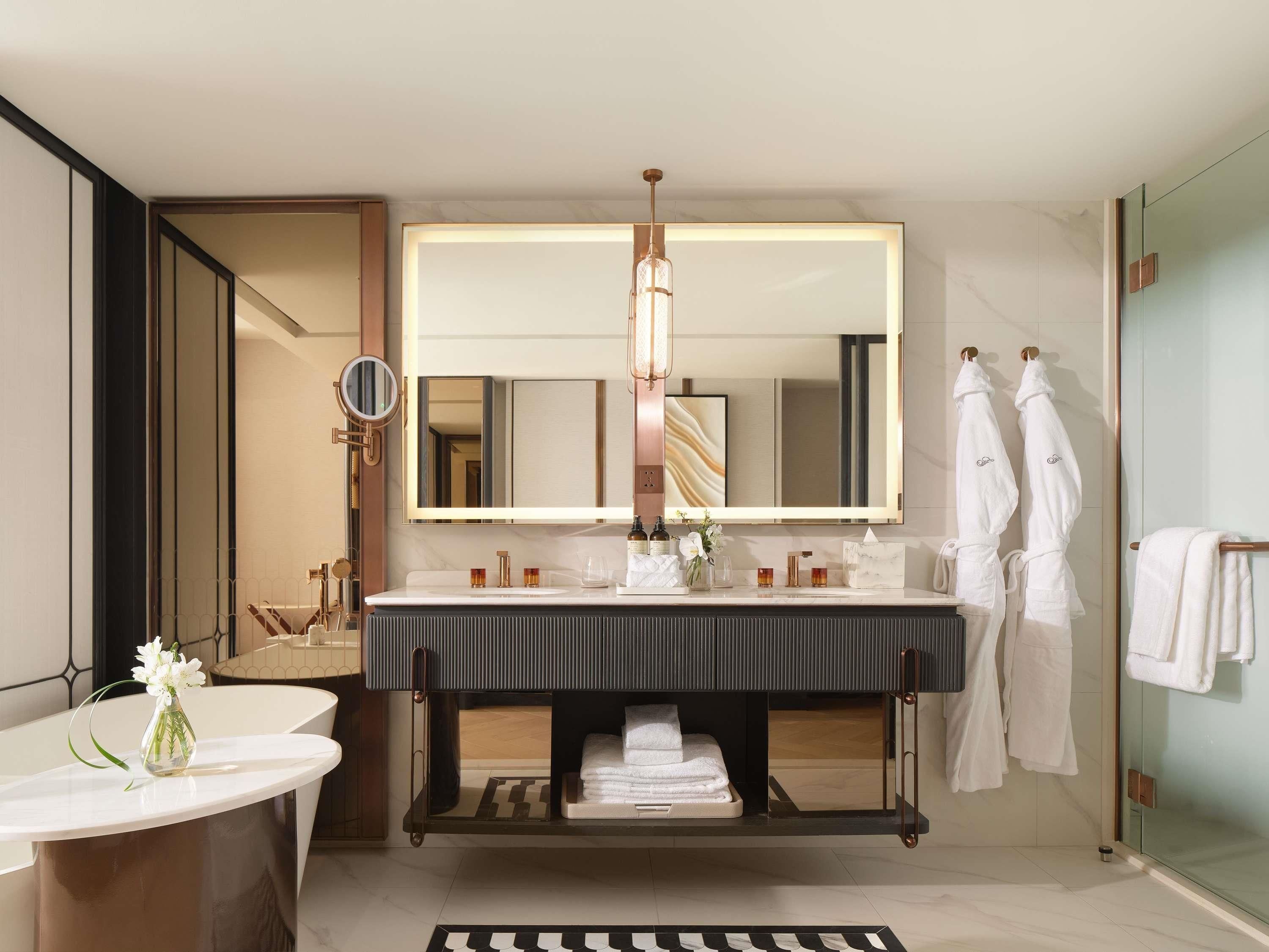 A modern bathroom with a large mirror, a vanity with a dark countertop, and two white towels hanging on hooks.
