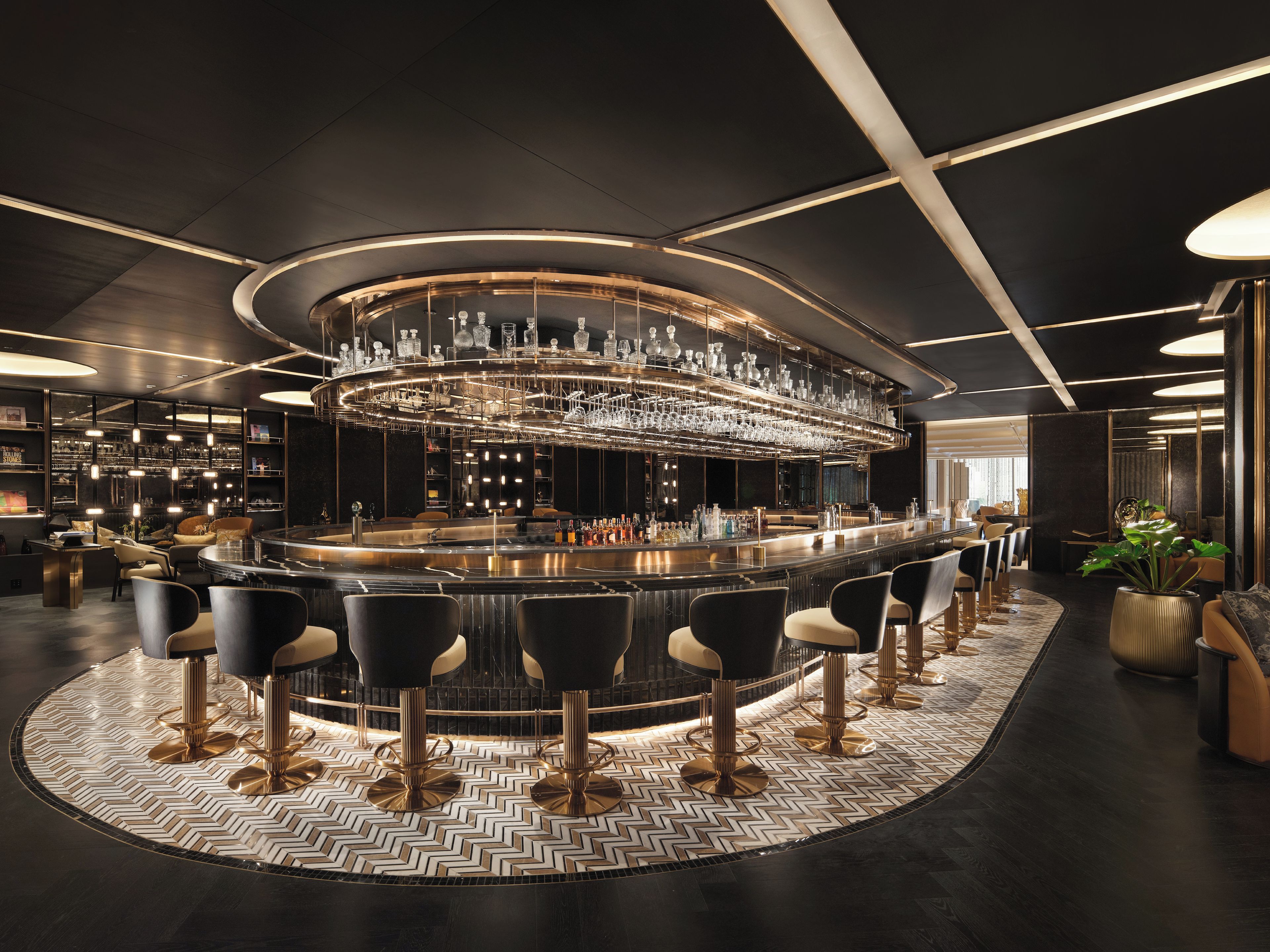 A modern bar area with a circular bar, multiple seating options, and a decorative ceiling light fixture.
