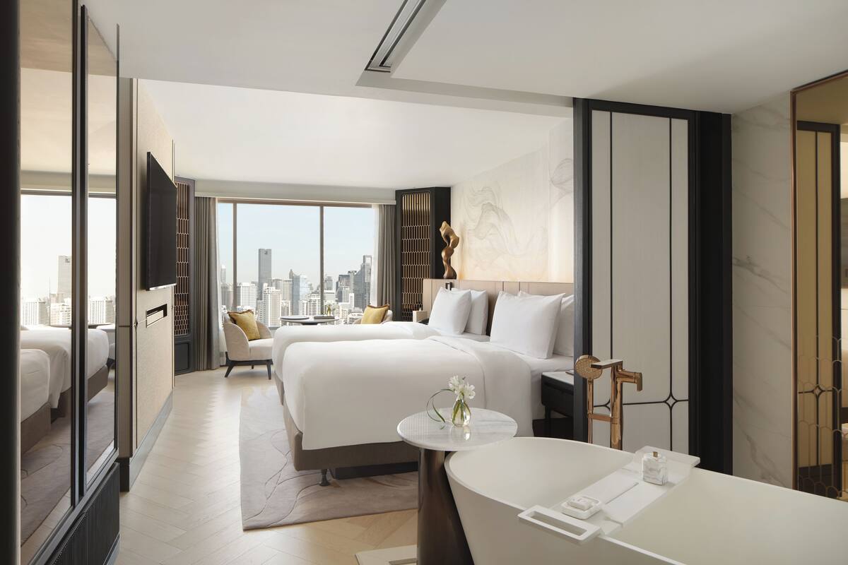 Ein modernes Hotelzimmer mit zwei Betten, einem großen Fenster mit Stadtblick, einem runden Tisch und einer Badewanne.