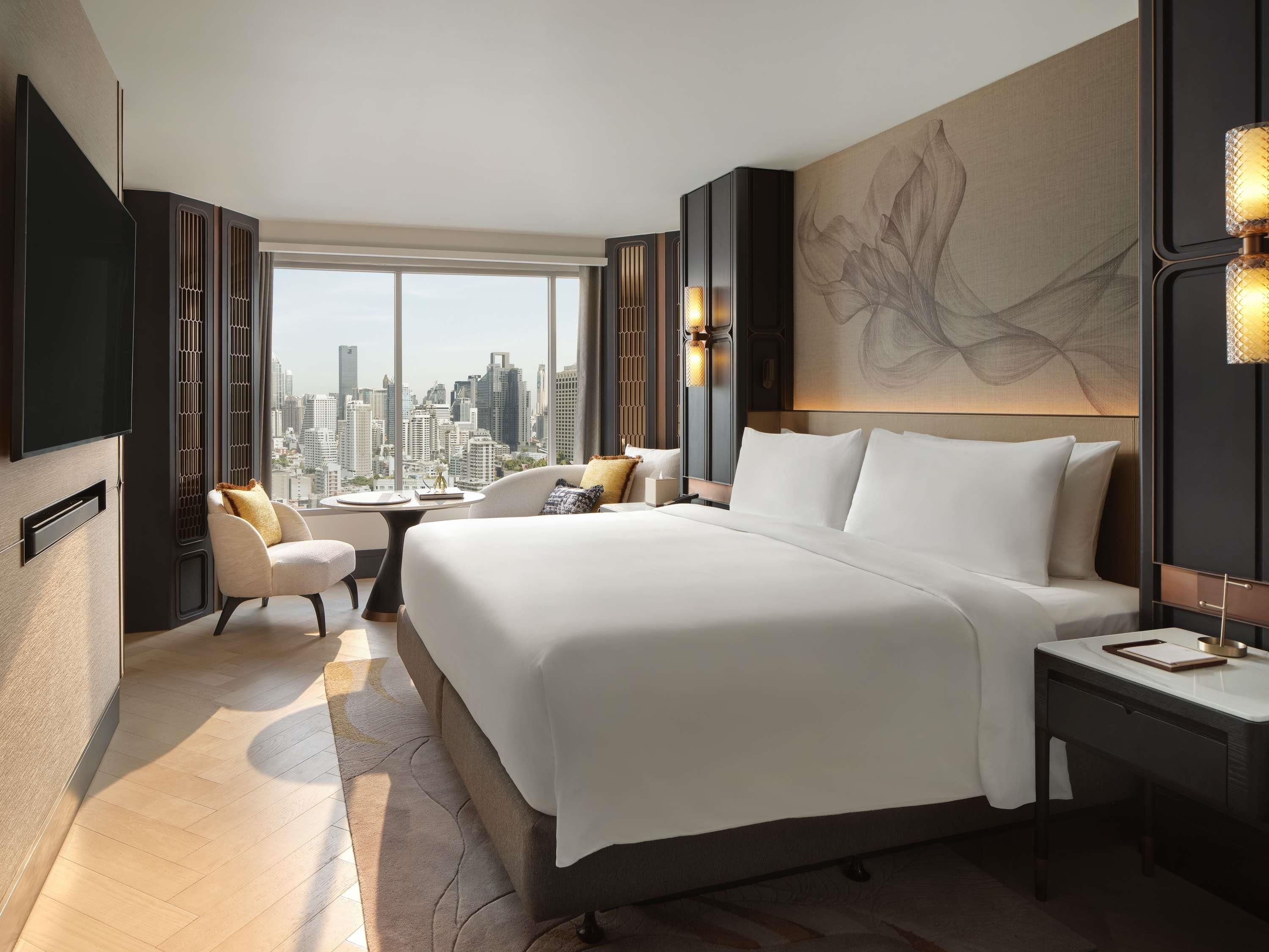 A modern hotel room with a large bed, a seating area, and a city view.