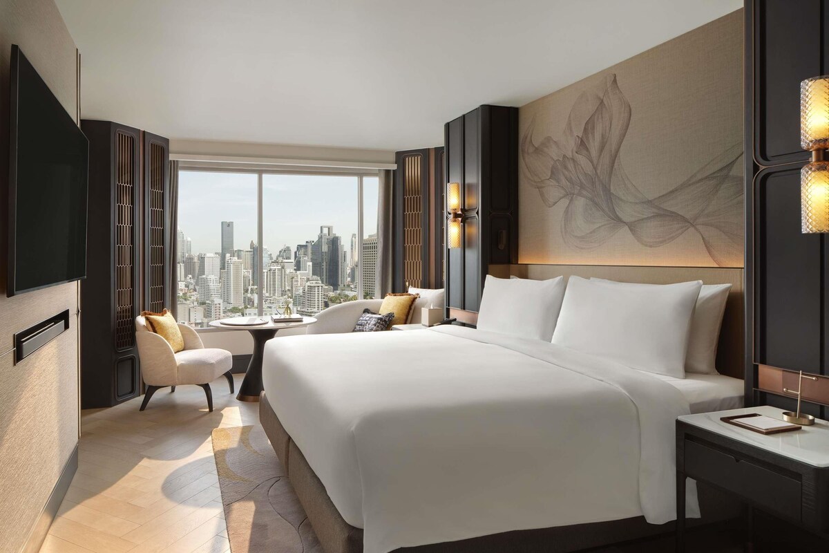 Ein modernes Hotelzimmer mit einem großen Bett, einer Sitzecke, einem Schreibtisch und Blick auf die Stadt.