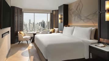 A modern hotel room with a large bed, a seating area, and a city view.