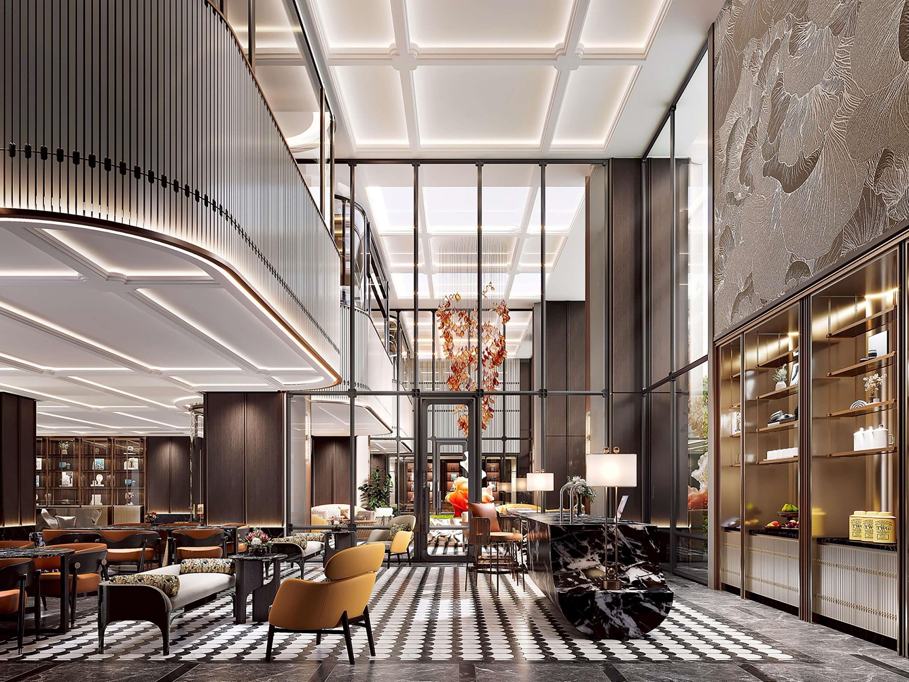 A spacious lobby with a high ceiling, a central staircase, and a seating area with sofas and tables.