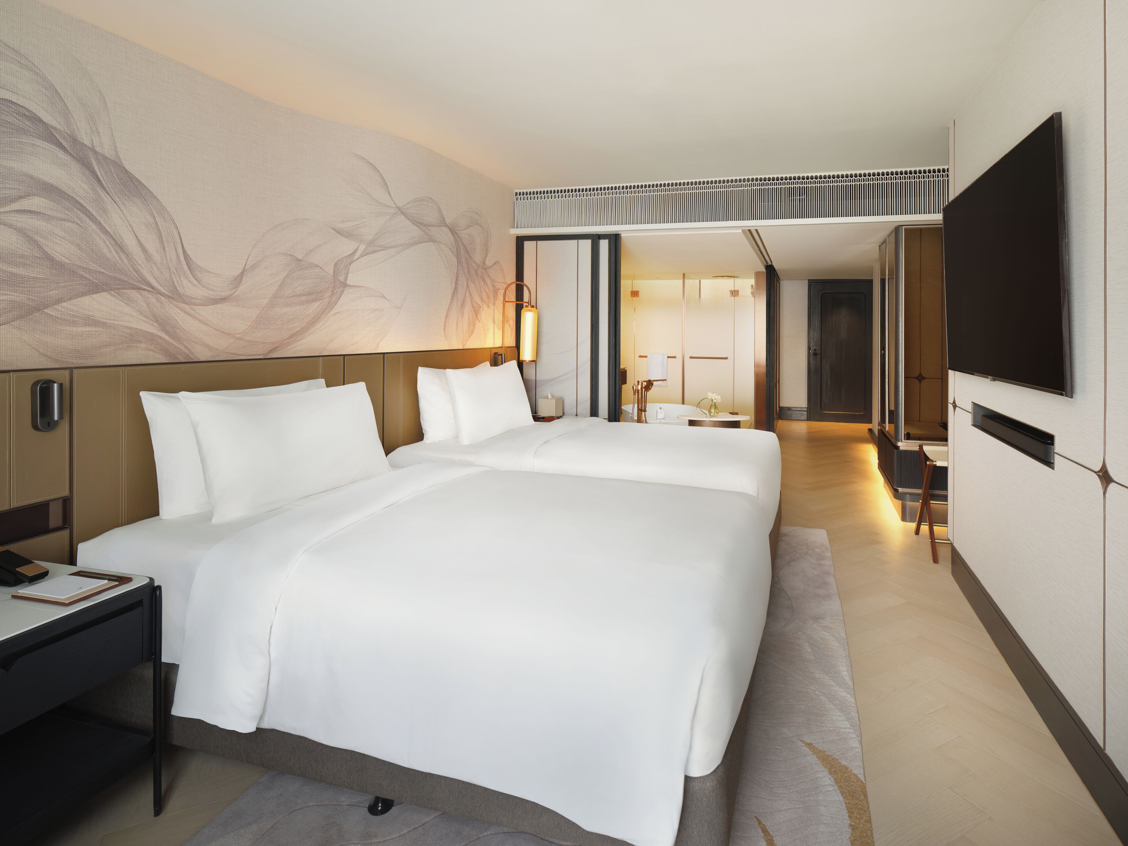 A modern hotel room with a large bed, bedside tables, a desk, a flat-screen TV, and a large abstract painting on the wall.