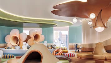 Una sala de estar moderna con un diseño arquitectónico único, que incluye una gran escultura de madera, un área de juegos con un túnel y vistas de la ciudad a través de amplios ventanales.