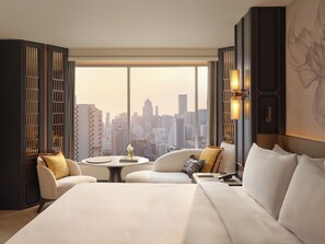 A modern hotel room with a large bed, two armchairs, a small table, and a city view. - Fairmont Bangkok Sukhumvit (Bangkok)