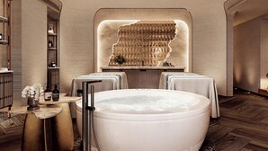 A modern spa room with a large bathtub, a wall-mounted massage table, and a shelf with toiletries. - Fairmont Bangkok Sukhumvit (Bangkok)