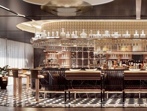Een bar met een rond zitelement, een vloer met patroon en een decoratieve wand met hangend servies.