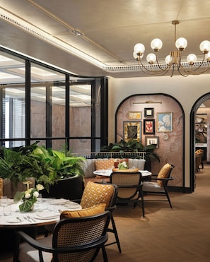 Een restaurantinterieur met ronde tafels, rieten stoelen en een kroonluchter.