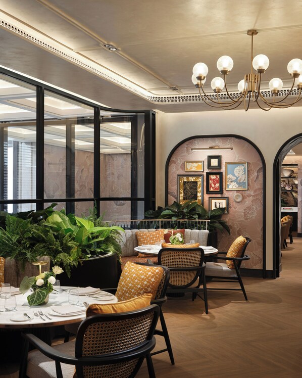 A restaurant interior with round tables, wicker chairs, and a chandelier. - Fairmont Bangkok Sukhumvit (Bangkok)