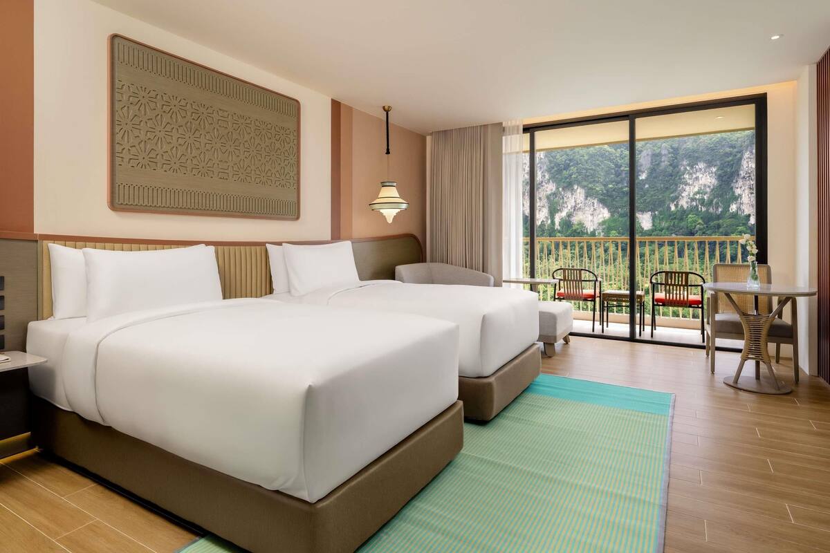 A hotel room with two beds, a balcony with a view, and a large decorative wall piece.