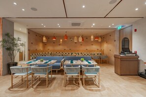Ein Restaurant mit einer langen Theke, verschiedenen Sitzmöglichkeiten, darunter eine große, blaue Couch und mehrere Tische mit Stühlen.