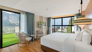 Ein modernes Hotelzimmer mit einem großen Bett, einem Balkon mit Bergblick, einer Sitzecke mit Stühlen und einem Fernseher.