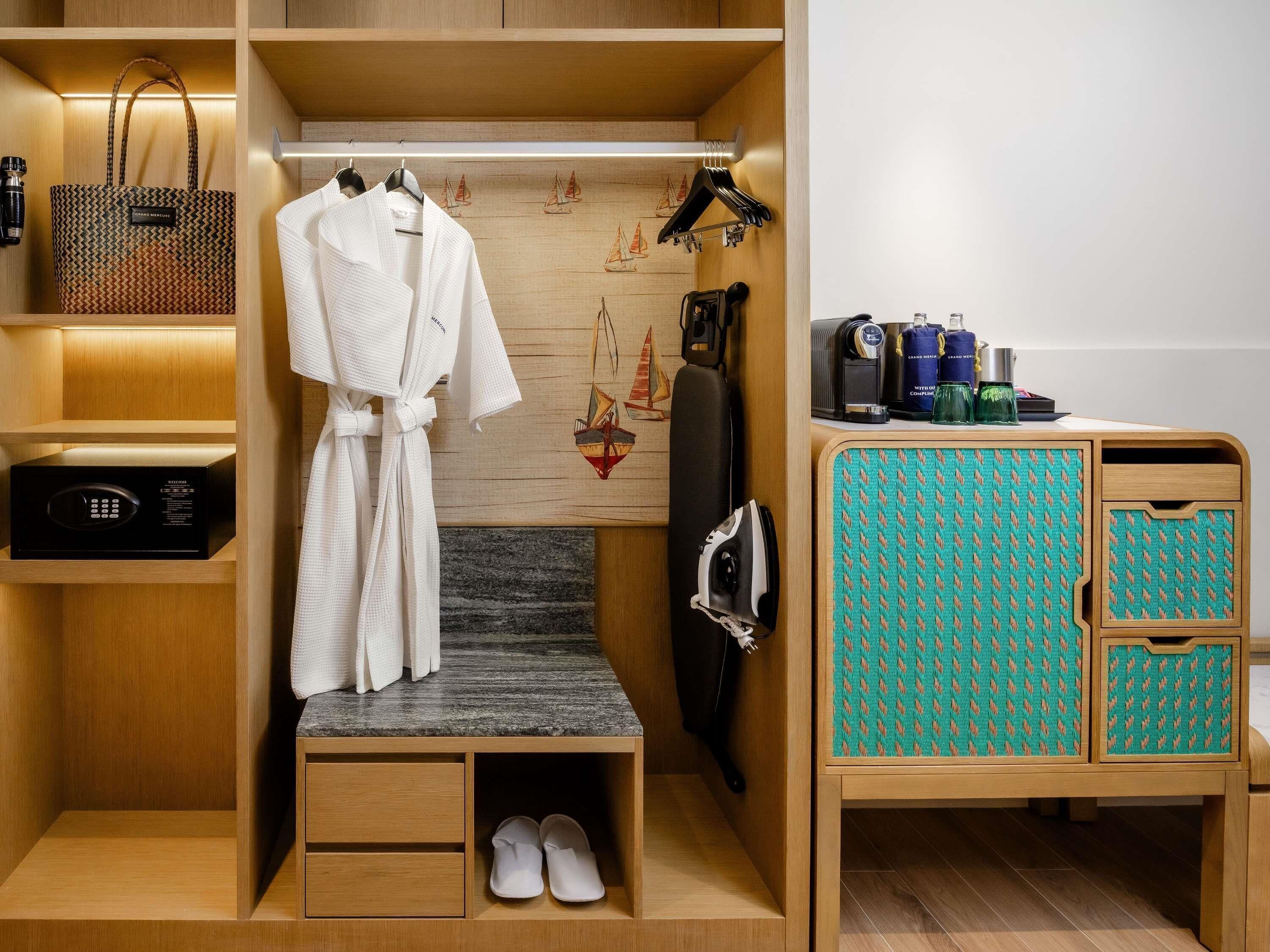Habitación de hotel compacta con vestidor, microondas, plancha pequeña y zona de estar con un aparador estampado.