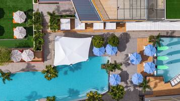 An aerial view of a resort with a swimming pool, sun umbrellas, lounge chairs, and a covered seating area.