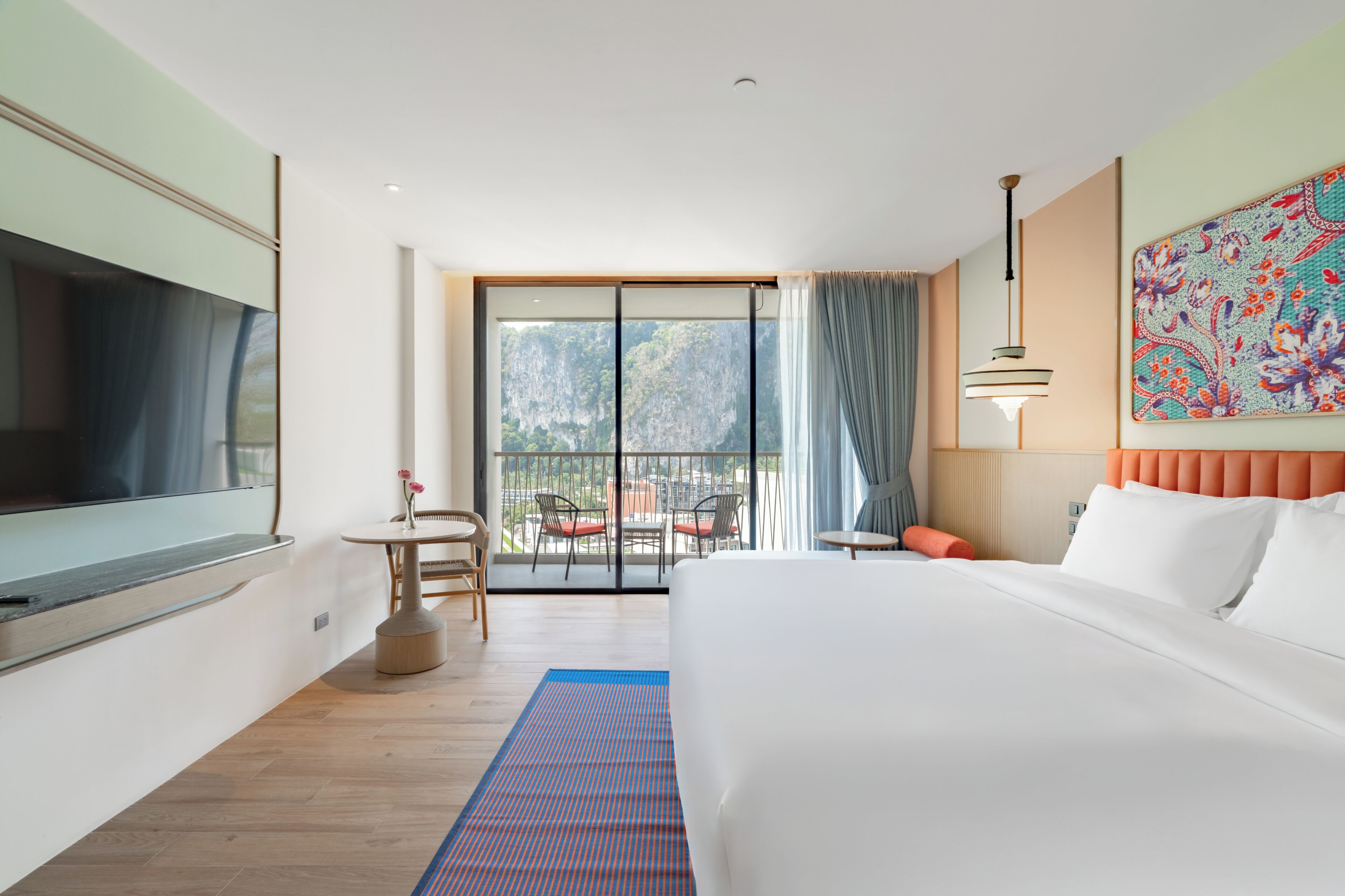 A hotel room with a large bed, a TV, a balcony with chairs, and a view of the mountains.