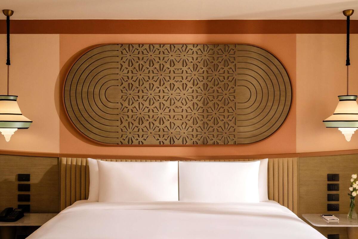 Ein Hotelzimmer mit einem großen Bett, zwei Nachttischen, einer dekorativen Wandverkleidung und zwei Pendelleuchten.
