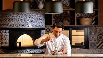 A chef preparing food in front of a blue-tiled oven with hanging lights.
