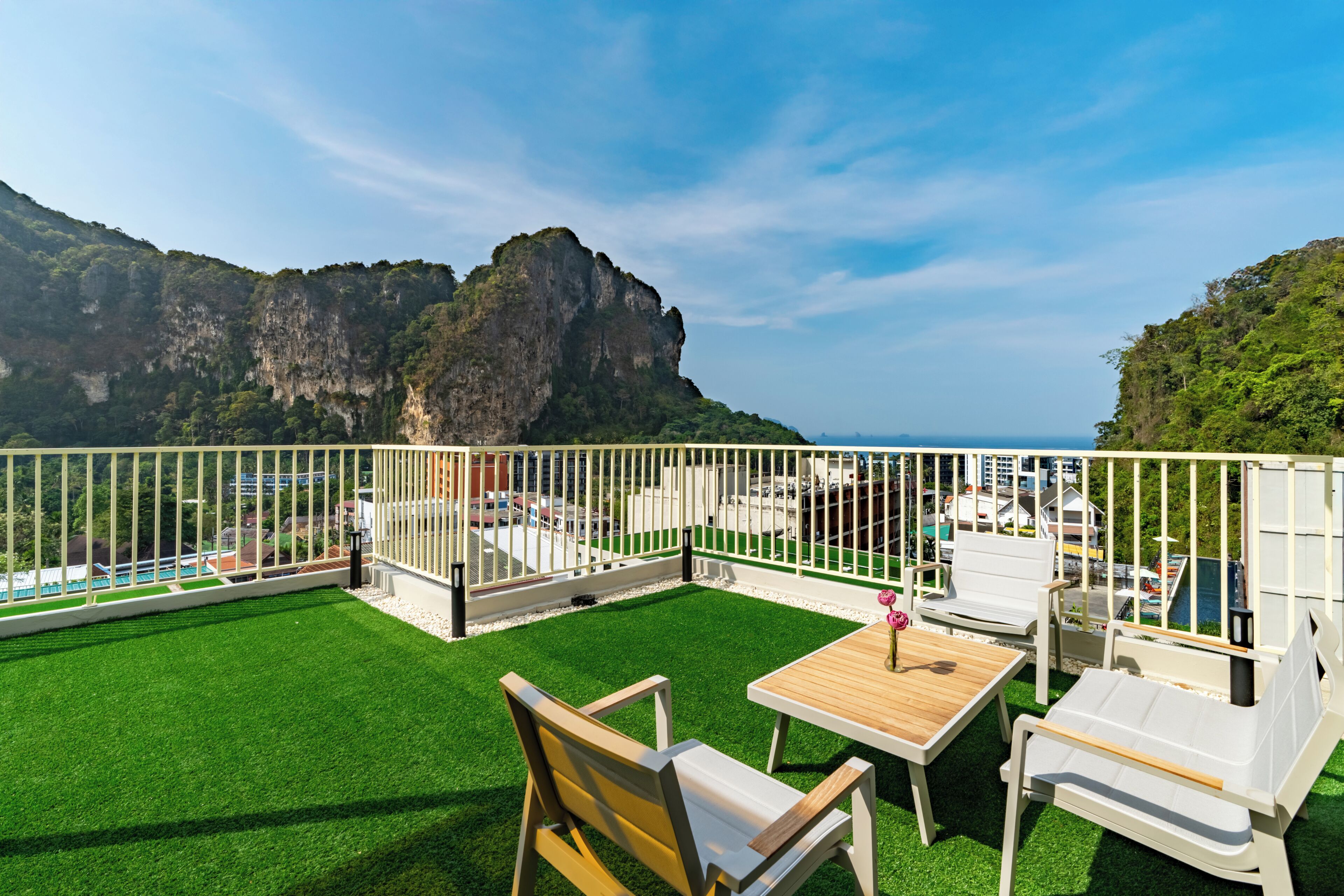 A balcony with a view of cliffs and the sea, furnished with white chairs and a wooden table.